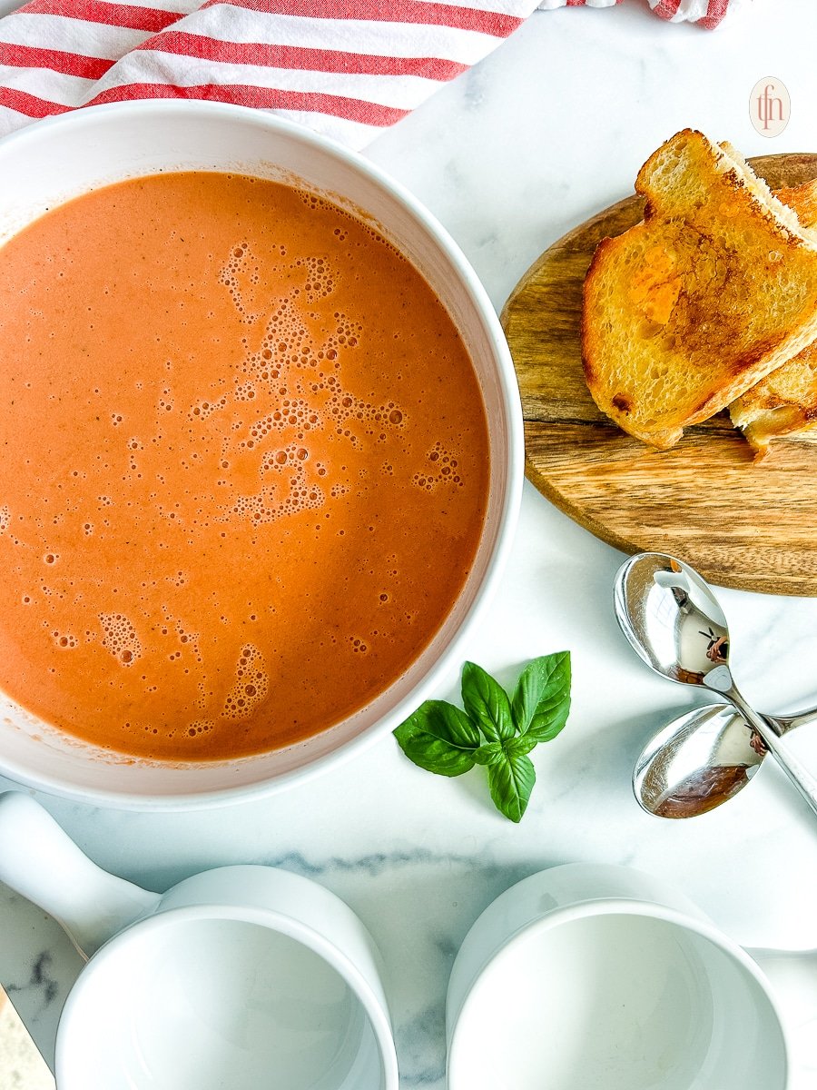 A white bowl filled with 3 ingredient tomato soup and a sprig of basil on the side.