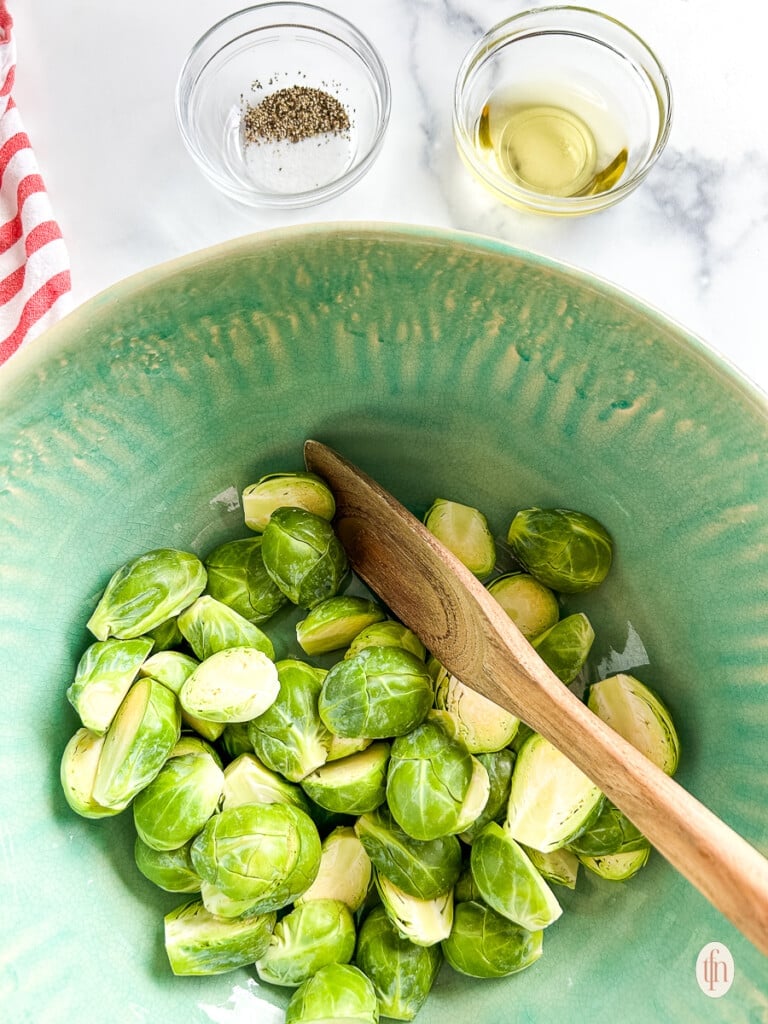 Sliced sprouts in a bowl stirred by a wooden spoon.