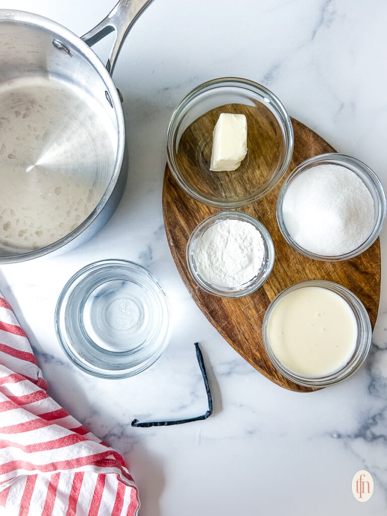 Ingredients for creamy vanilla sauce in small bowls on a white background.