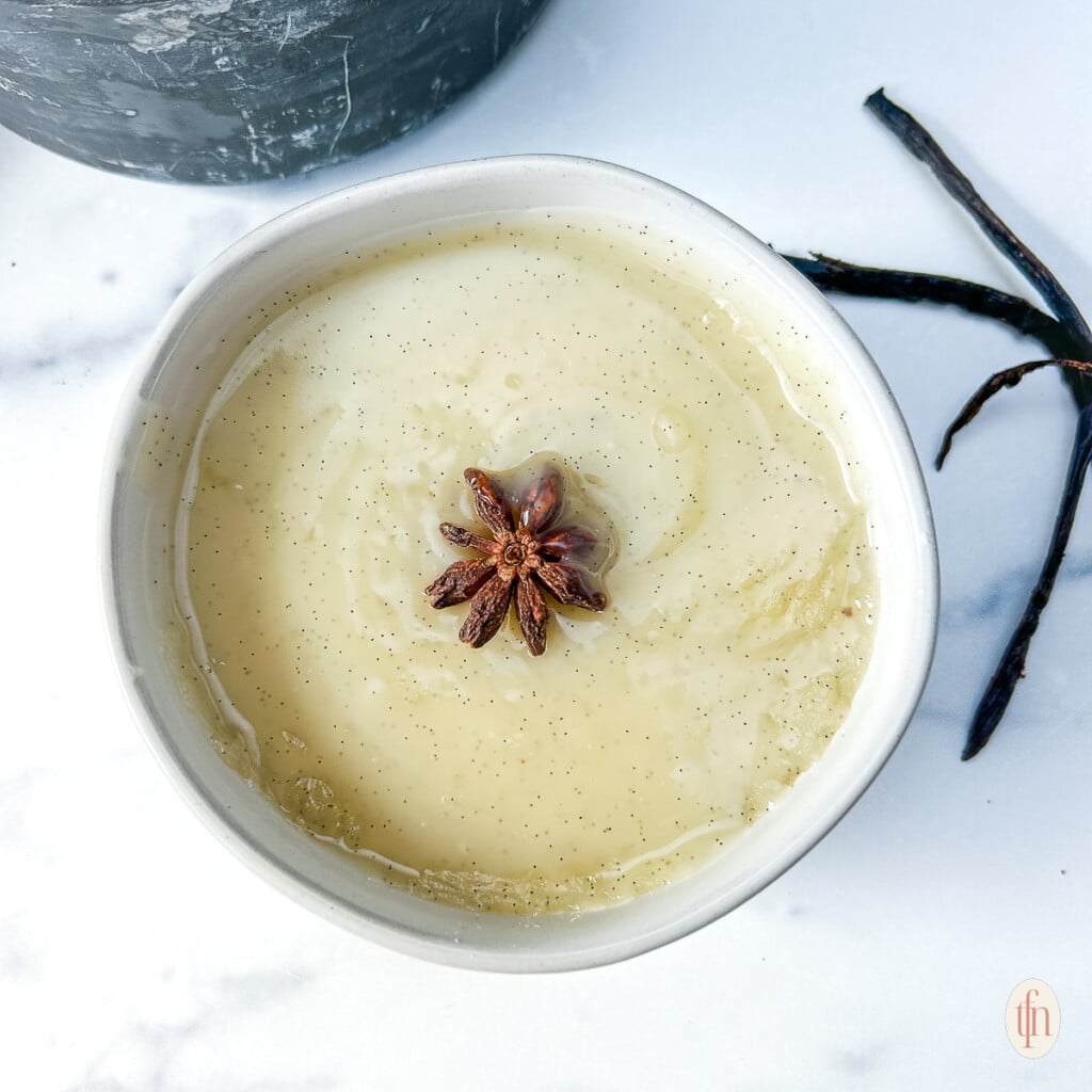 Creamy vanilla sauce garnished with star anise, in a small white bowl.