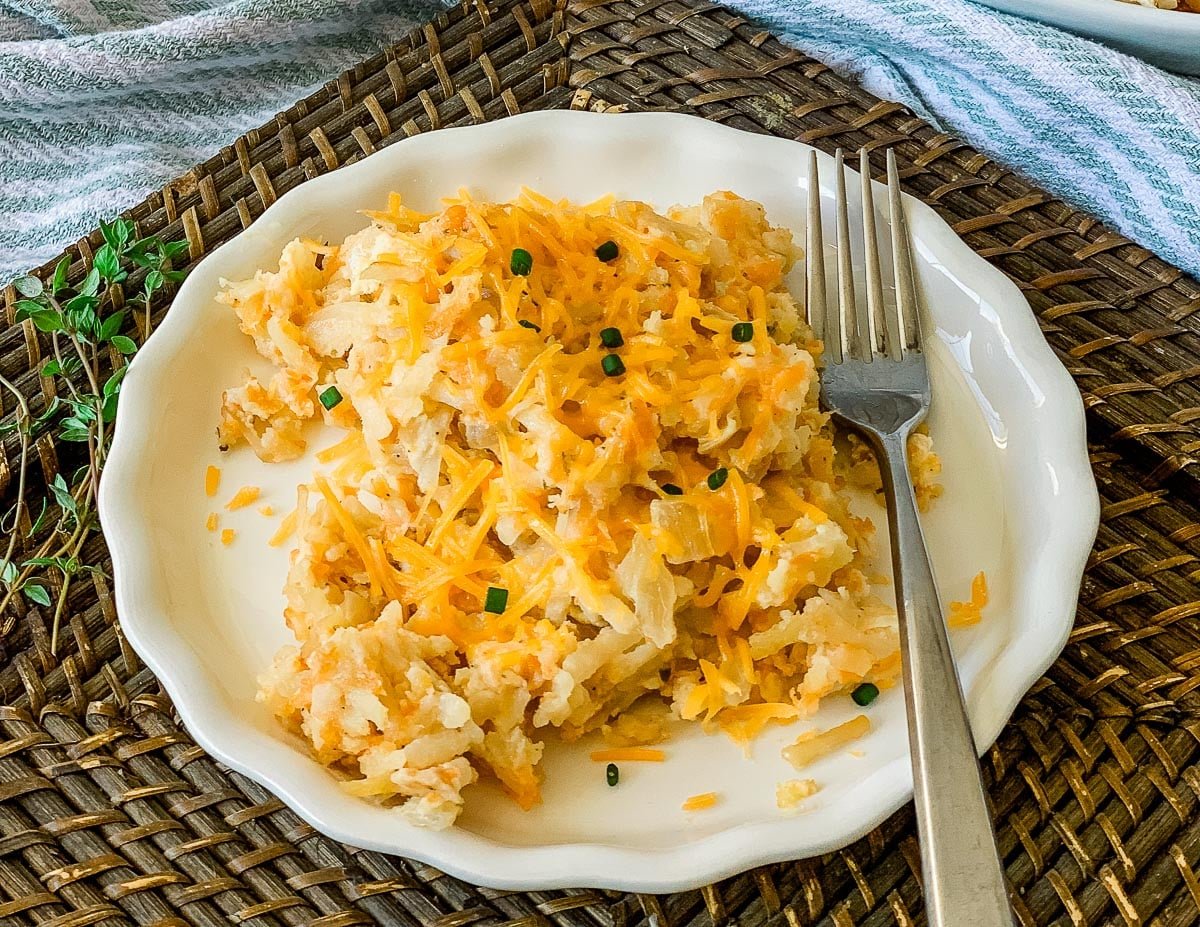 A small plate of finished dish: crock pot cheesy hashbrown casserole, with a fork.