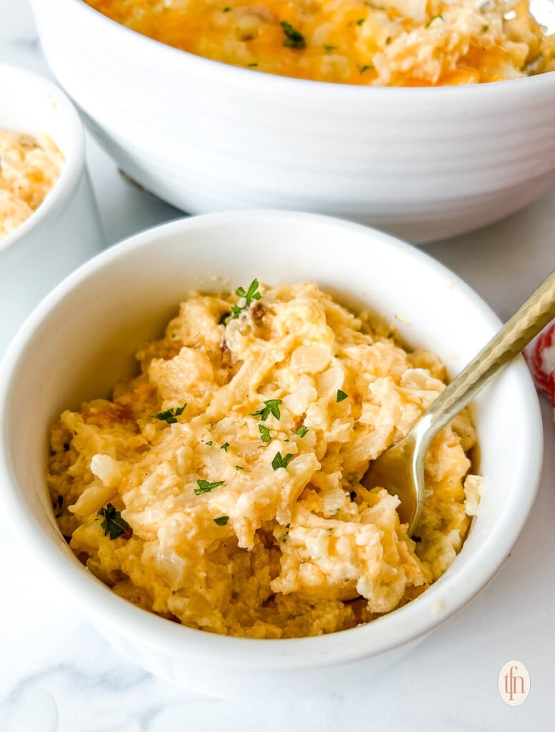 Serving size of crockpot funeral potatoes in a small bowl with a spoon.