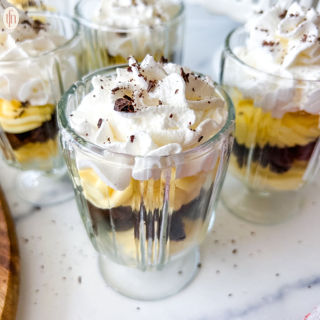 Four glass cups filled with chocolate bread, pudding, and topped with whipped cream.