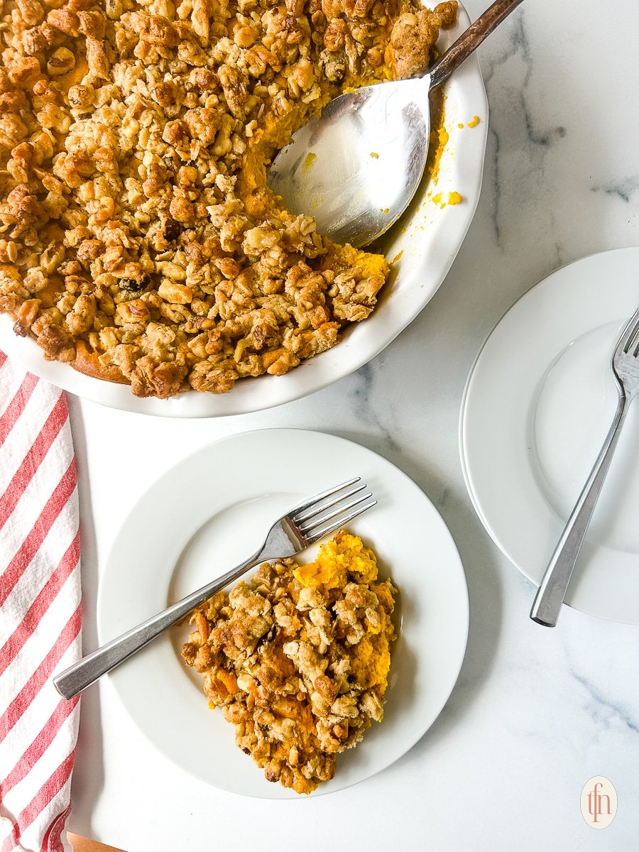 A plate of carrot casserole with a fork next to the whole serving dish with a spoon.