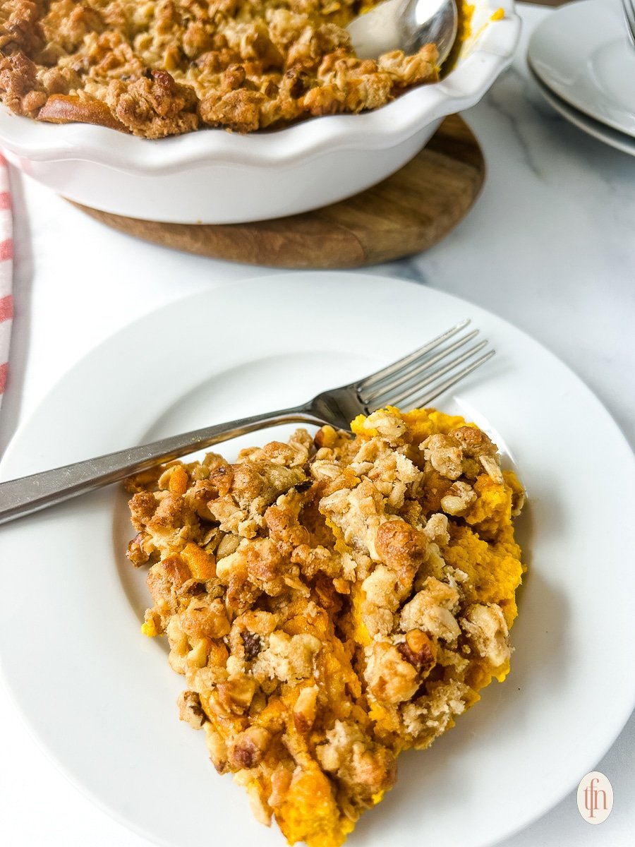 A white plate with a serving of carrot casserole with a fork.