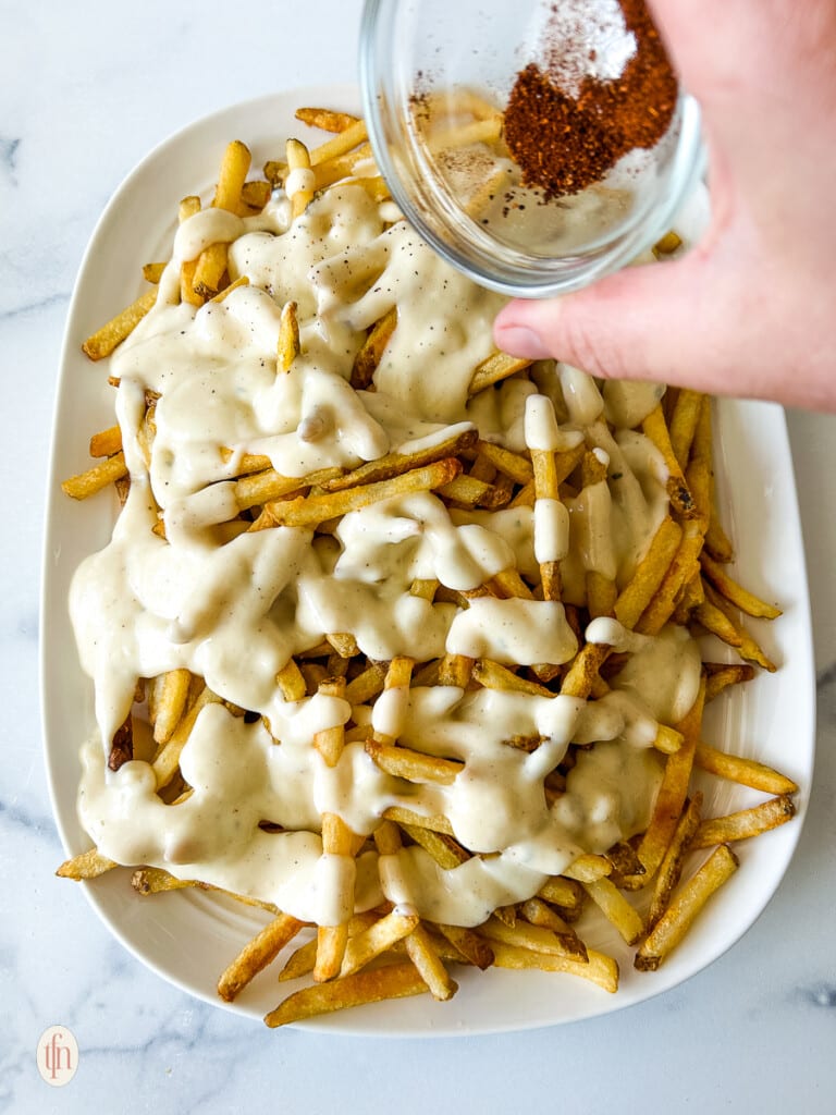 Pouring spices over the top of cheesy fries.
