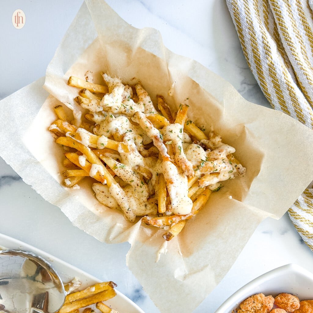 A basket filled with fries covered in sauce on a white background.