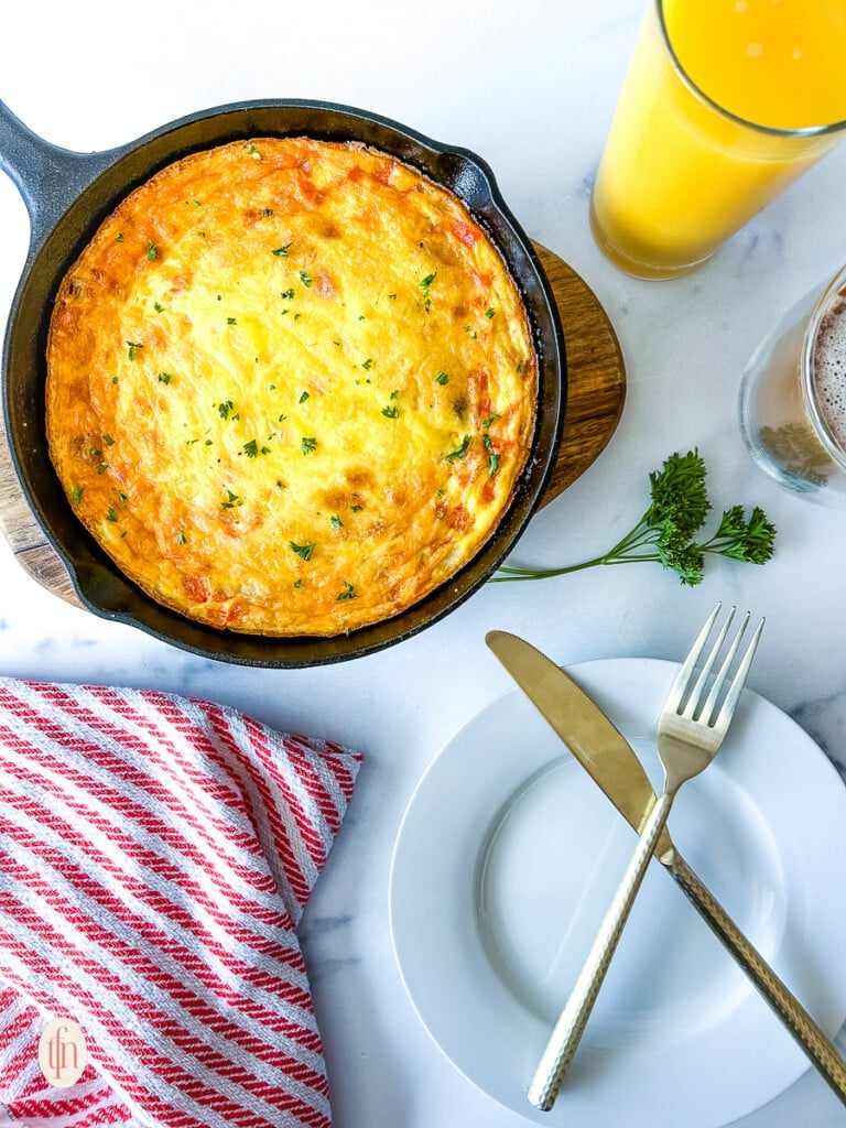 Fully cooked frittata in a skillet next to a plate with silverware.