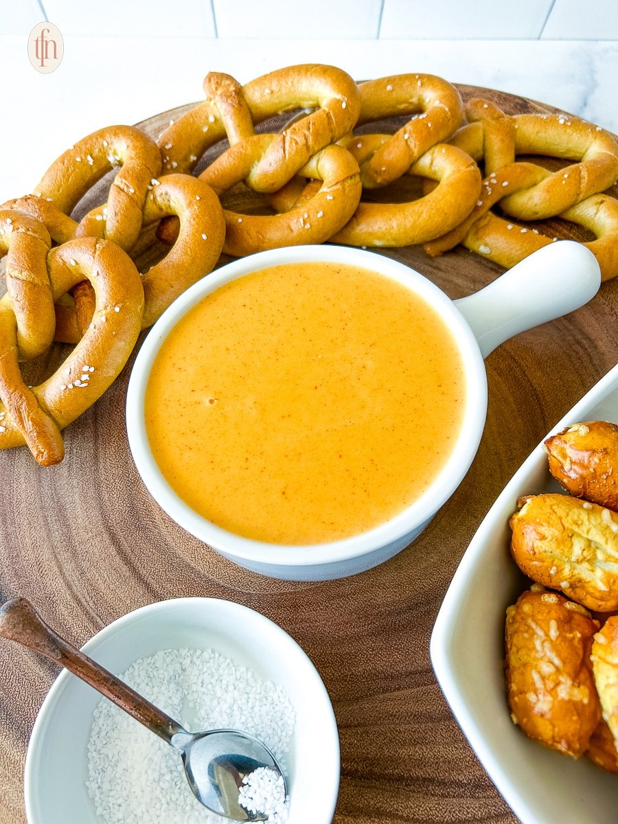 A serving bowl of pretzel cheese dip next to pretzels and a bowl of salt.