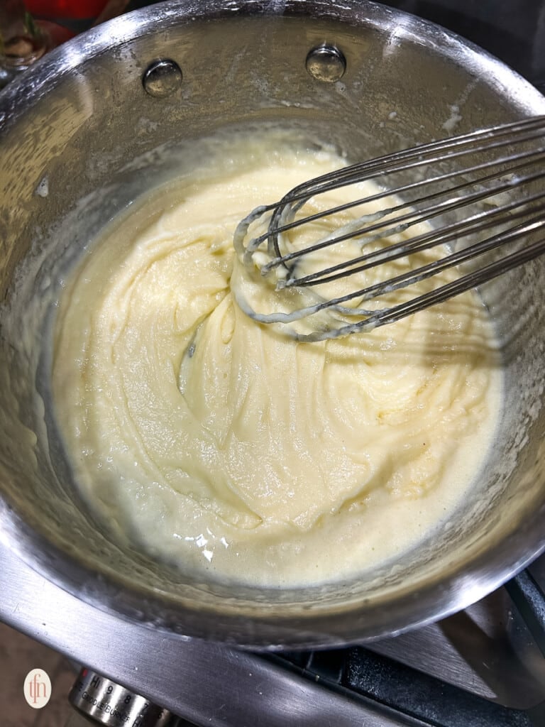 A whisk combining butter, flour, and chicken broth into a sauce.