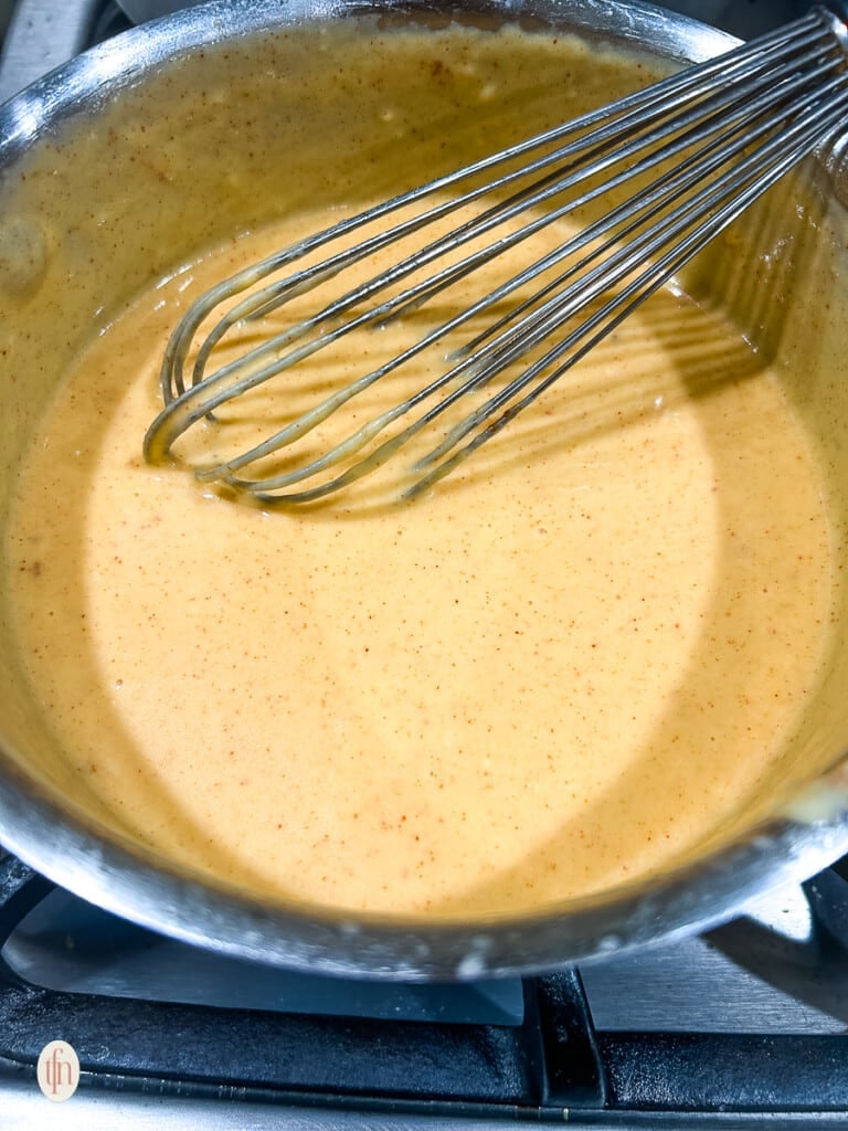 A whisk stirring up pretzel cheese sauce.