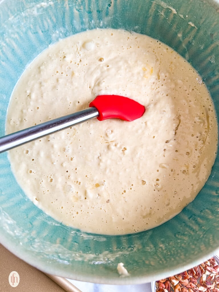 Mixing the batter with a red silicone spatula in a blue bowl.
