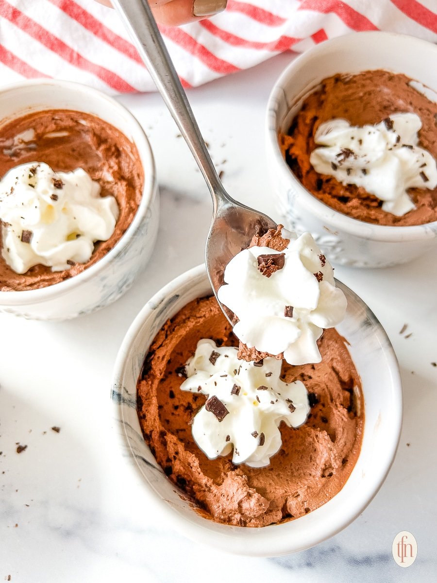 Spoon lifting whipped cream and mousse from a small bowl.