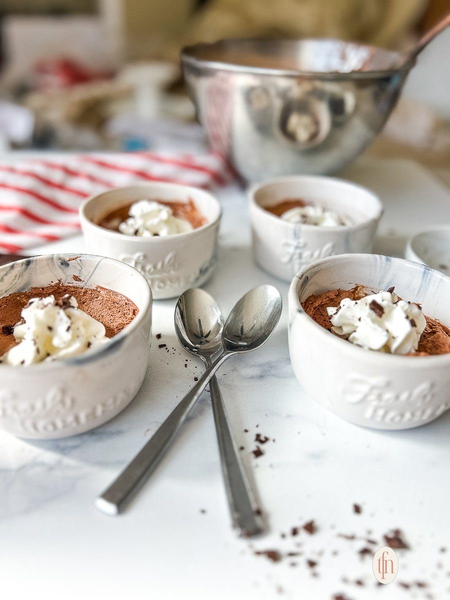 Individual cups filled with chocolate mousse and topped with whipped cream and shaved chocolate on a white background.