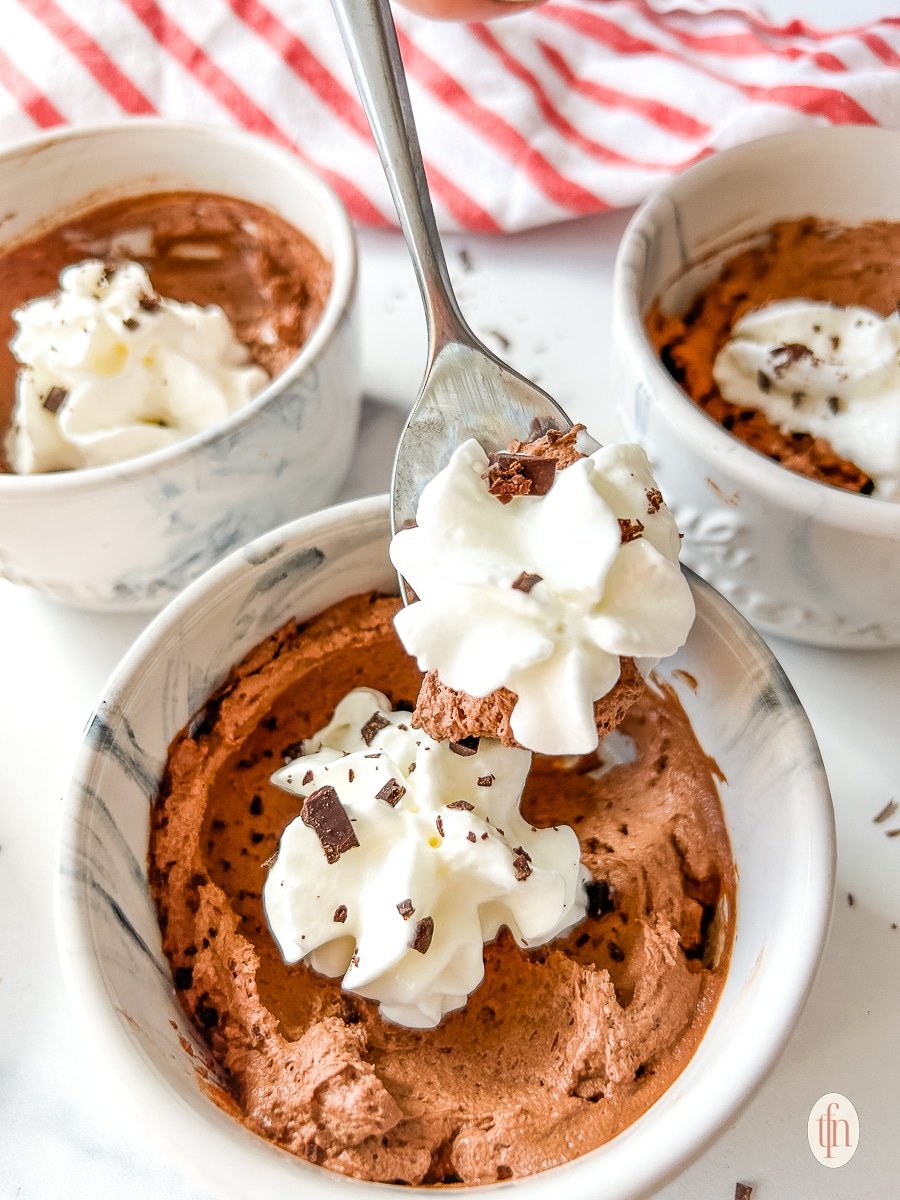 Spoon lifting whipped cream and mousse from a small bowl.