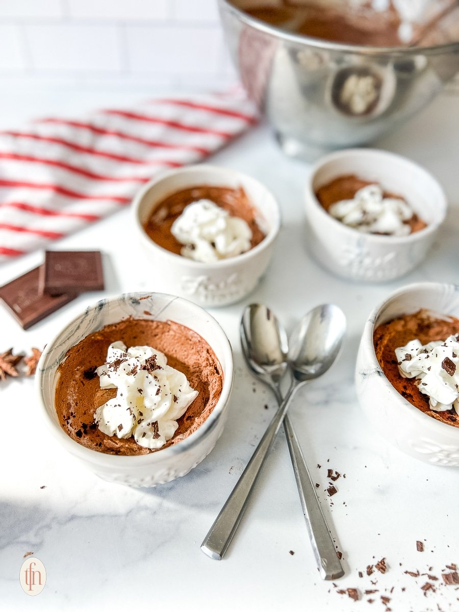 Individual cups filled with chocolate mousse and topped with whipped cream and shaved chocolate on a white background.