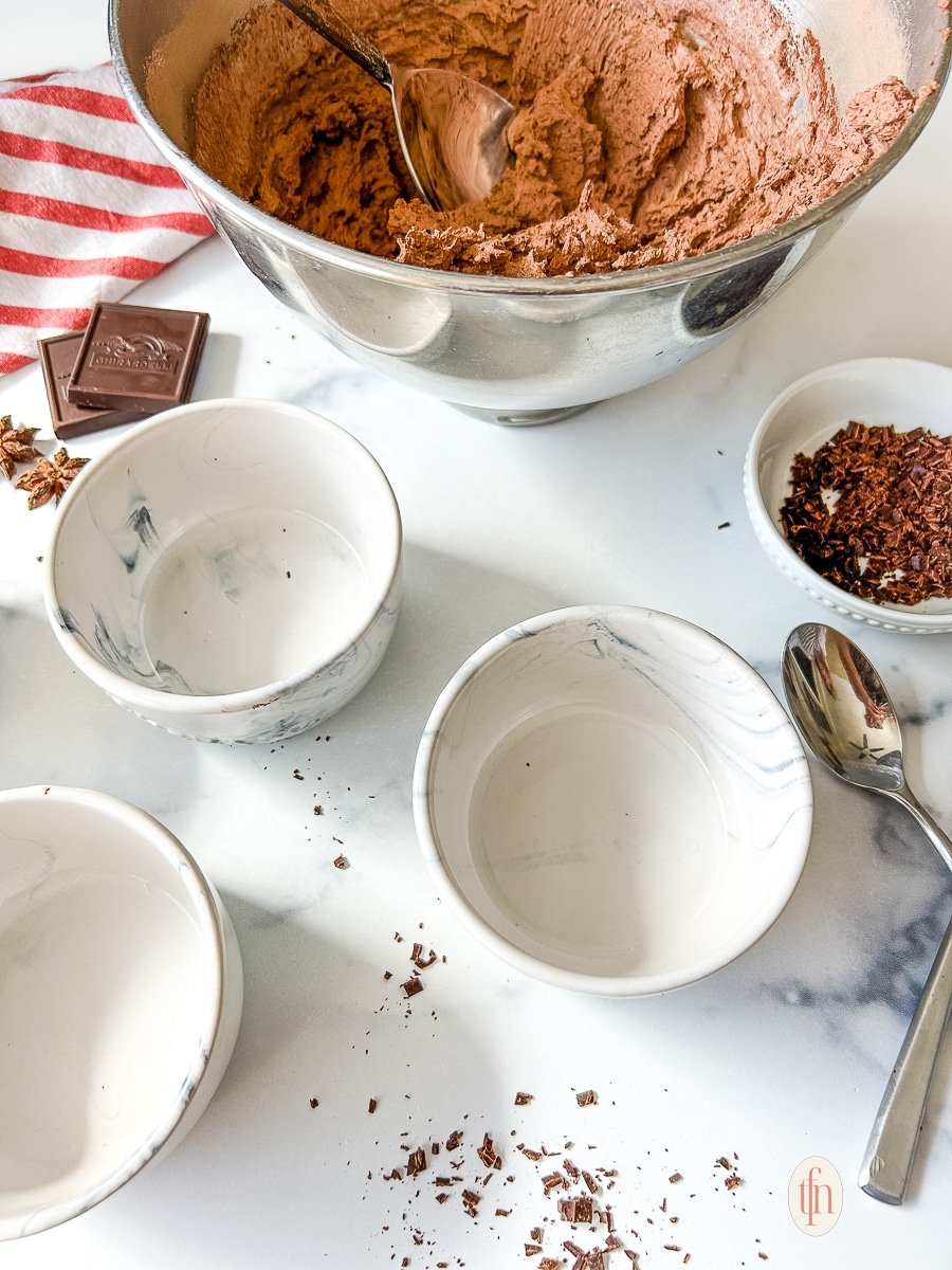 A bowl of mousse and three empty ramekins.