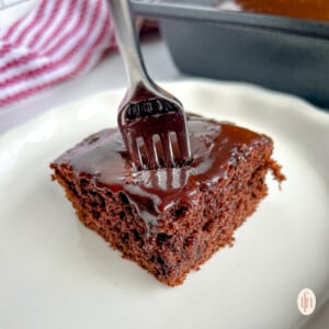 Fork stuck into a slice of a frosted chocolate dessert.