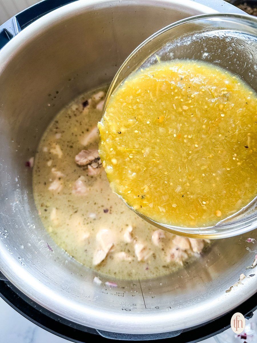 Pouring chicken broth into an Instant Pot filled with diced chicken.