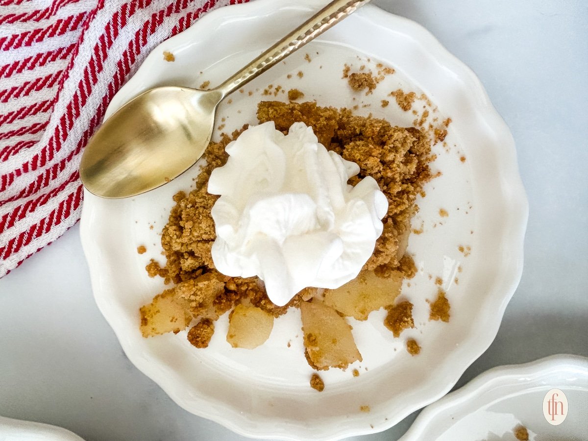 Pears and whipped cream on a white plate with a spoon on top.