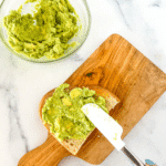 Using a spatula to schmear guacamole onto a slice of toast.