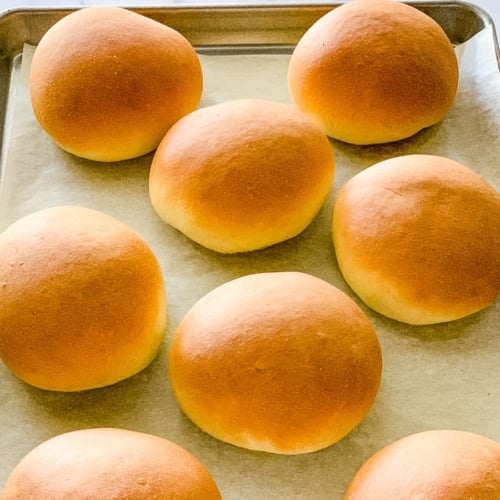 Homemade burger buns on a baking sheet.