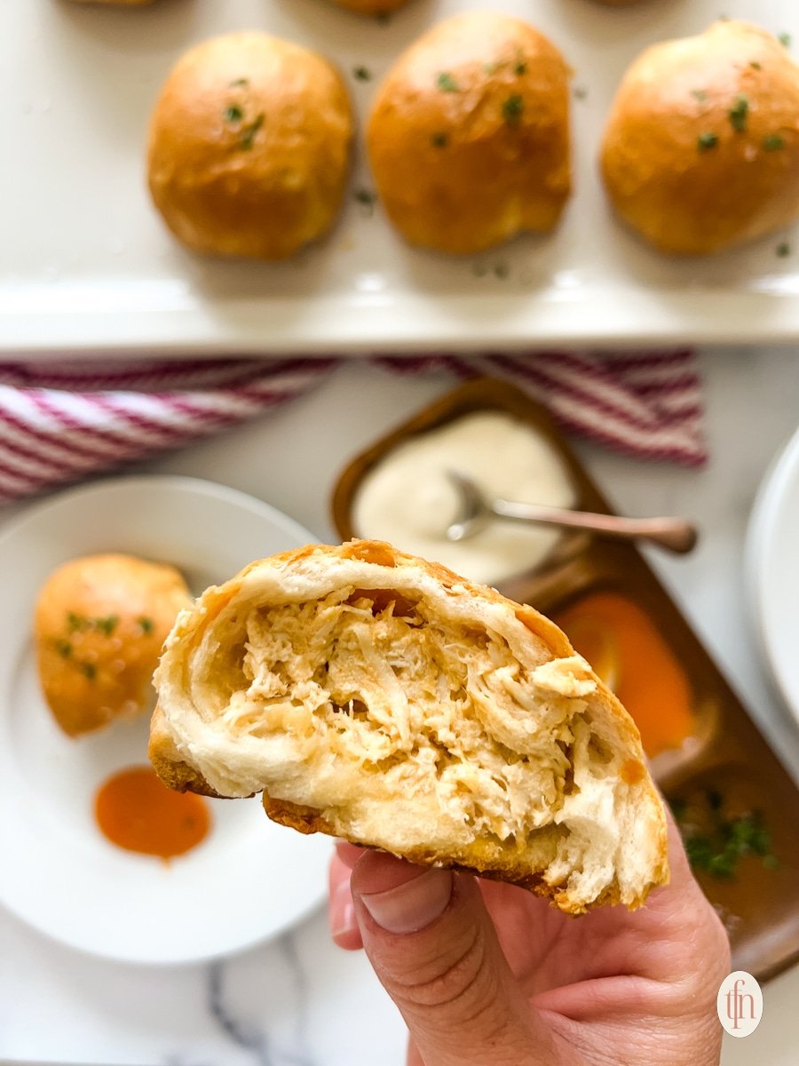 Holding one half of a chicken ball over a plate and dish filled with condiments.