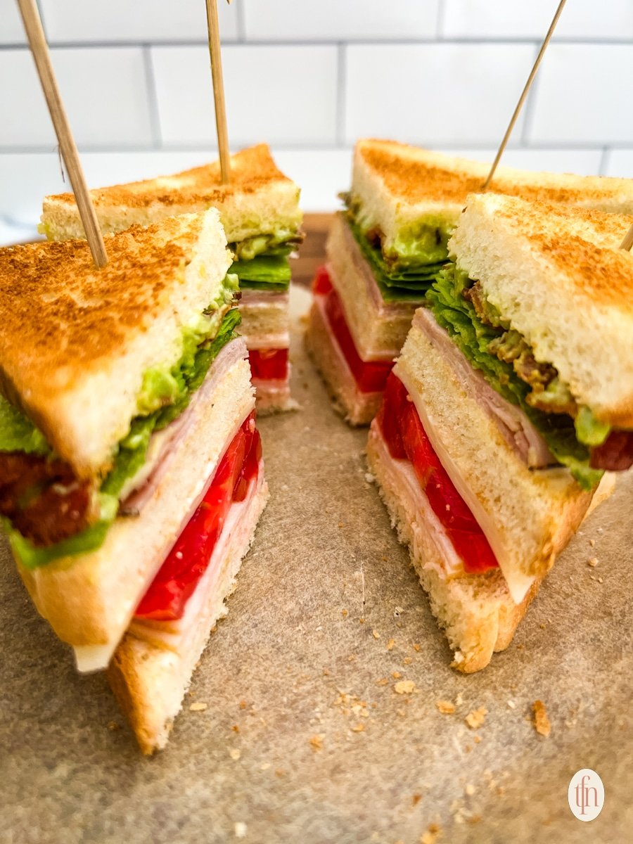 Four slices of a chicken club sandwich with stick on it, placed on parchment paper.