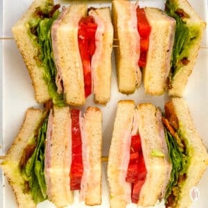 Four slices of chicken club sandwich on a white plate.