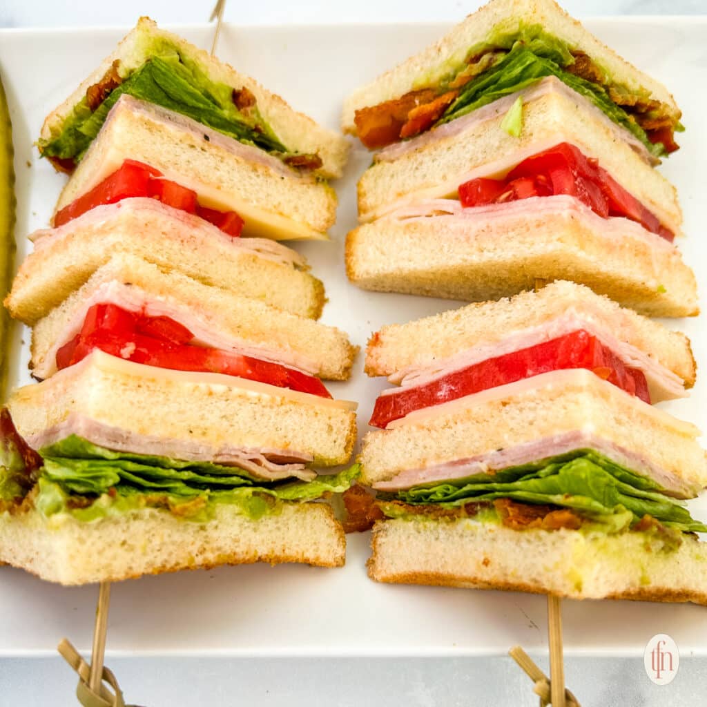 Four slices of a chicken club sandwich with sticks on a white plate.