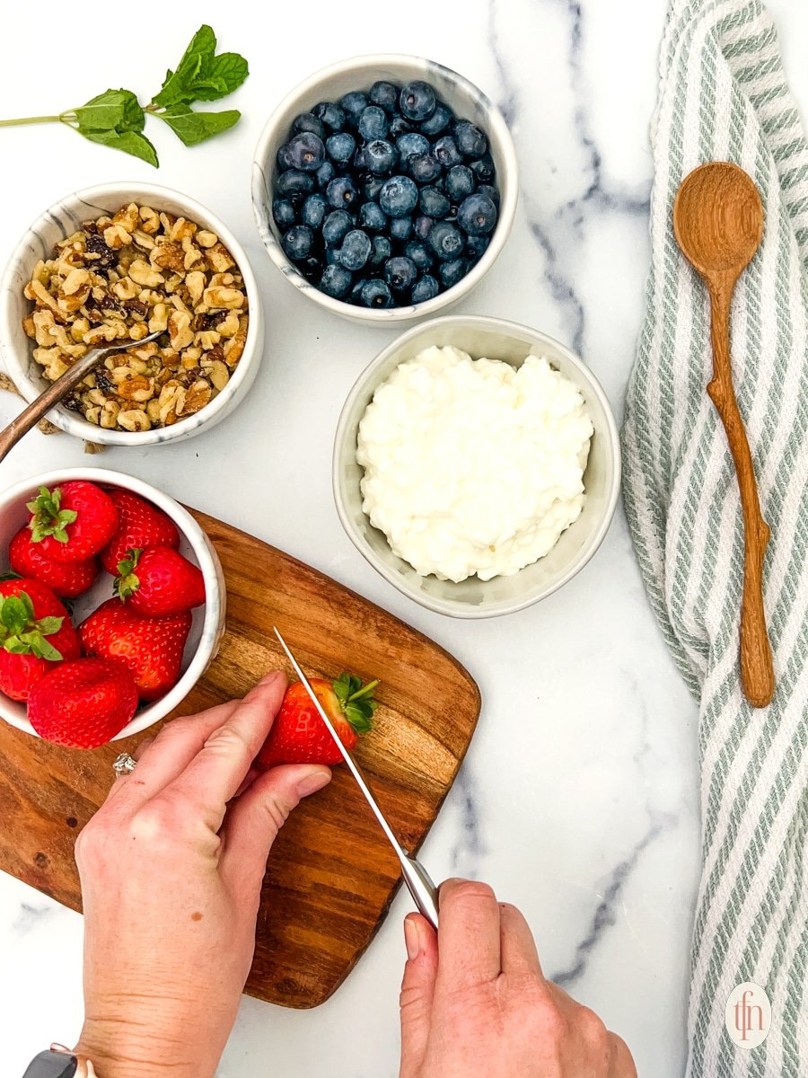 Slicing strawberries with prepared ingredients for cottage cheese and fruit bowls.