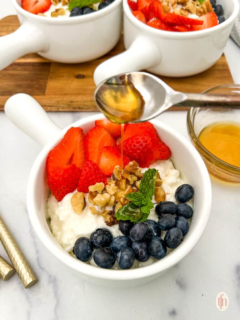 Adding honey on top of cottage cheese and fruit bowl.