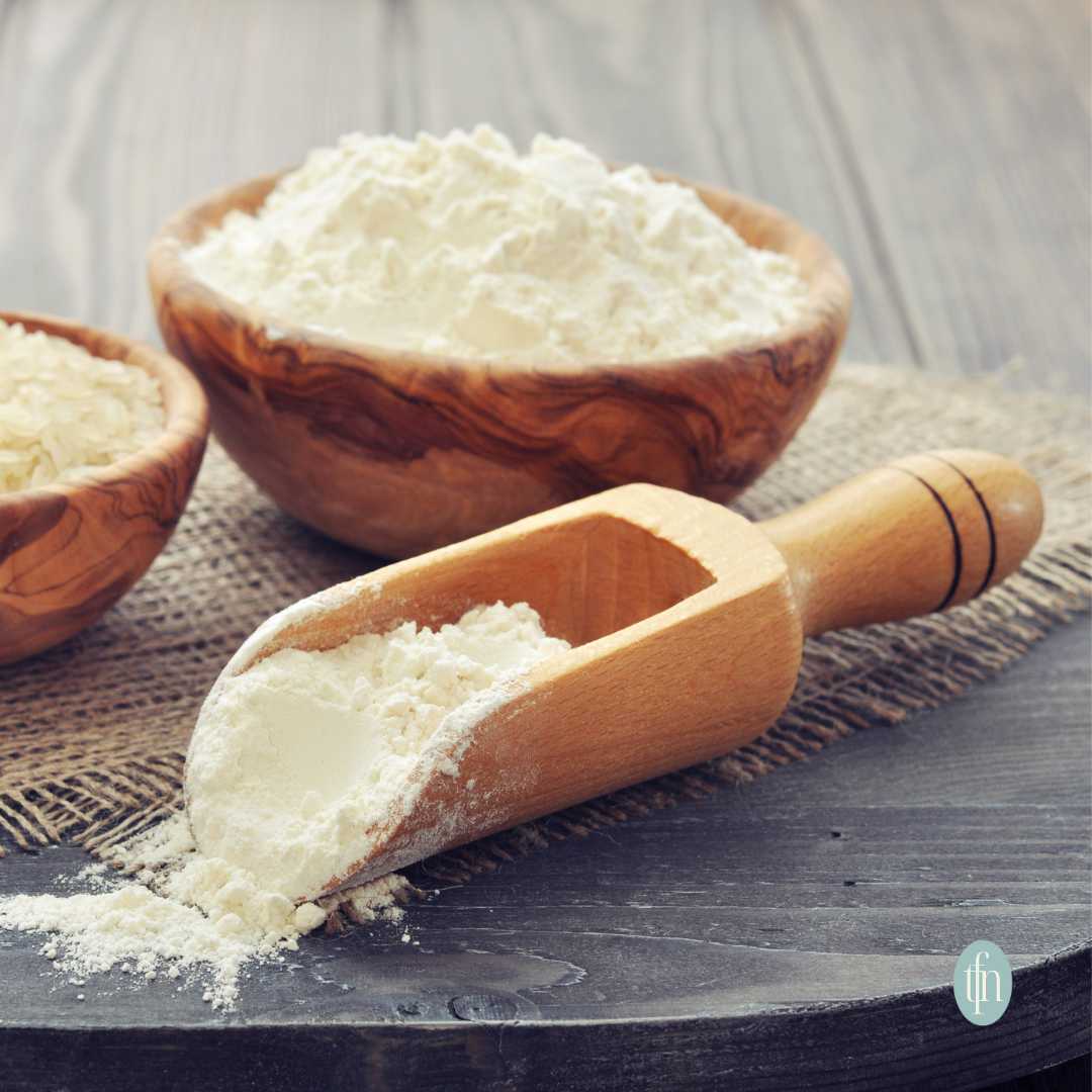 Self rising flour in a wooden scoop and a wooden bowl, sitting on a piece of burlap.