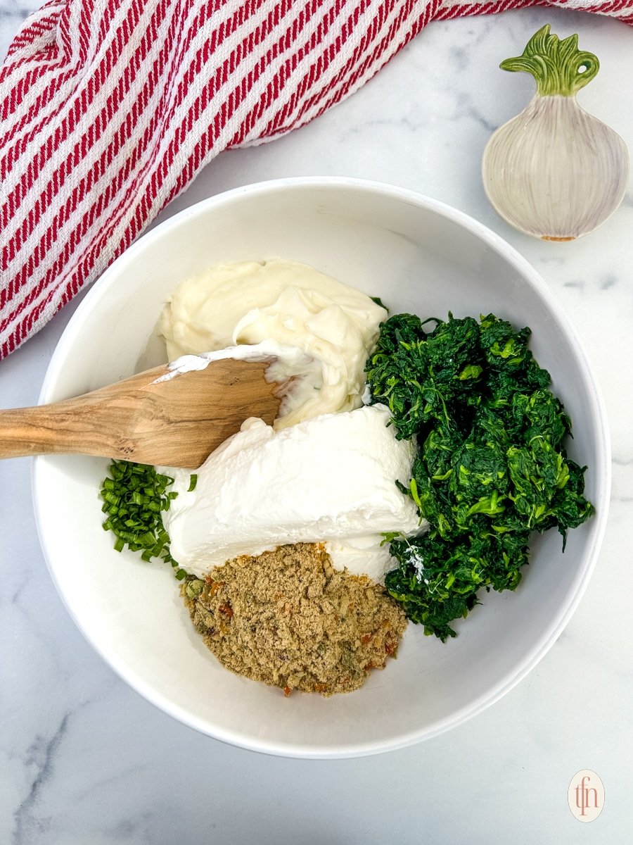 Ingredients for Knorr spinach dip in a mixing bowl with a wooden spoon.