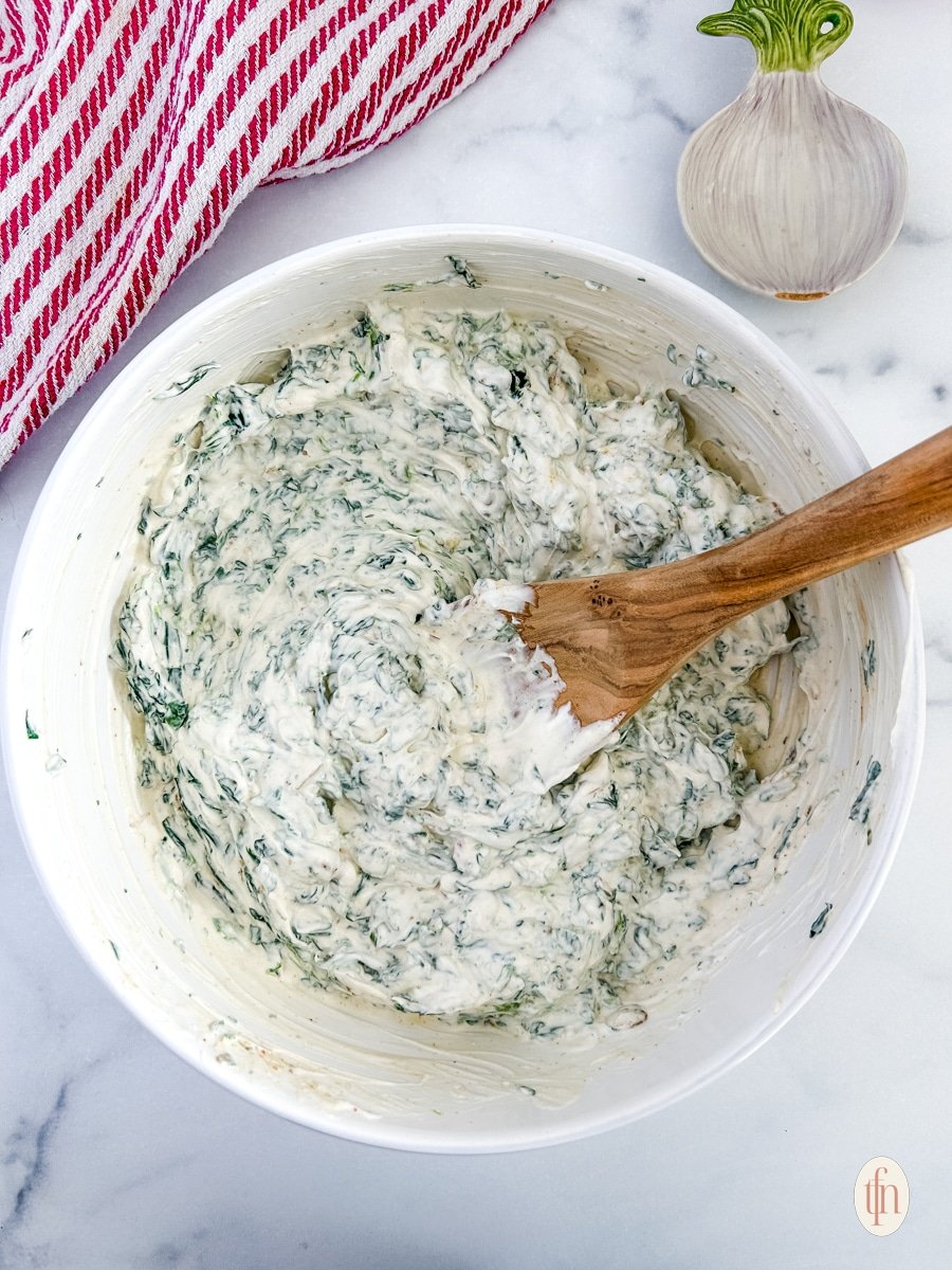 Knorr spinach dip in a mixing bowl with a wooden spoon.