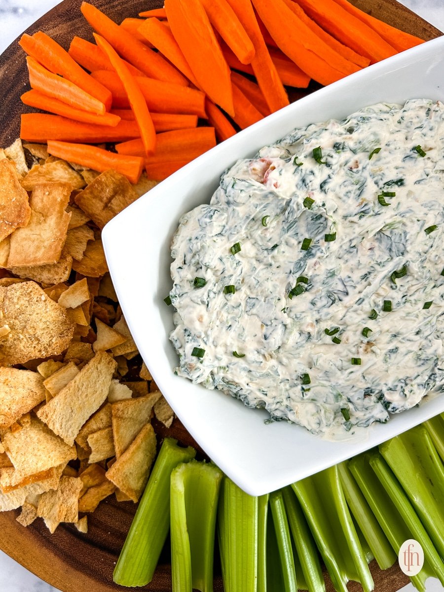 Knorr spinach dip on a serving rectangular bowl. Served on top of a round wooden board with crackers and vegetables.