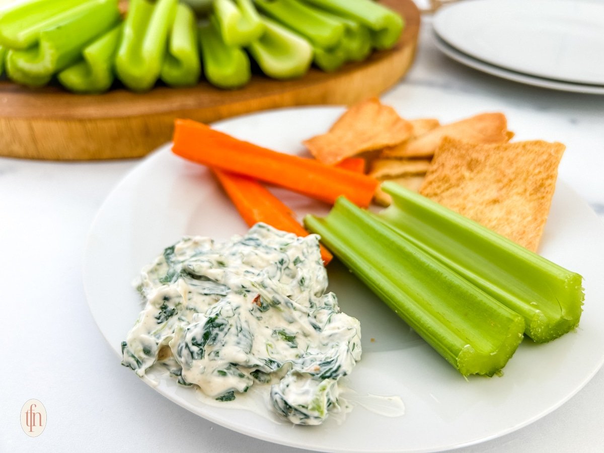 A plate of spinach dip, vegetables and crackers.