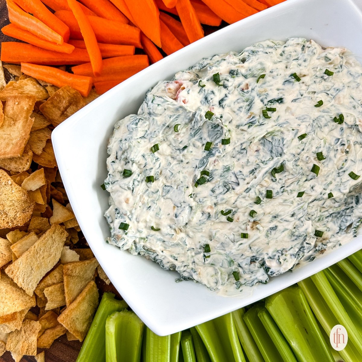 Knorr spinach dip on a serving rectangular bowl. Served on top of a round wooden board with crackers and vegetables.