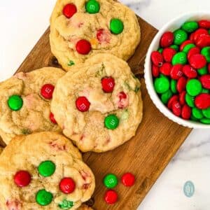 4 homemade Christmas cookies with red and green M&Ms, sitting next to a bowl full of M&M candies.