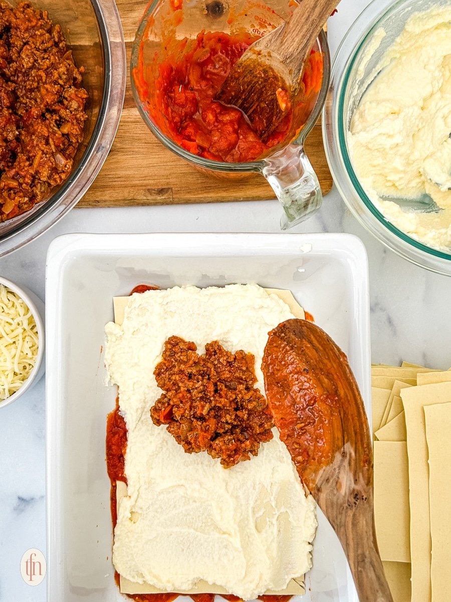 Assembling no boil low sodium lasagna on a white pan with prepared ingredients.