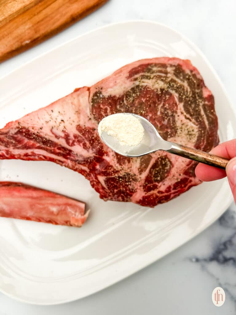 A spoon with powder with a plate of cowboy ribeye.
