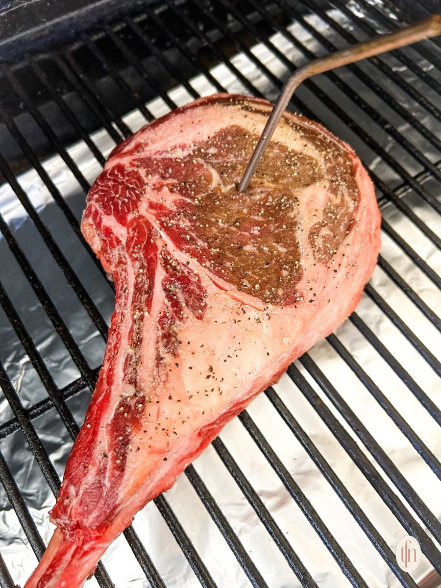 Digital meat thermometer inserted in a raw cowboy ribeye placed on a griller.