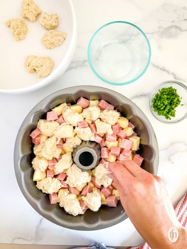 Adding dough into the pan to make monkey bread with ham and brie.