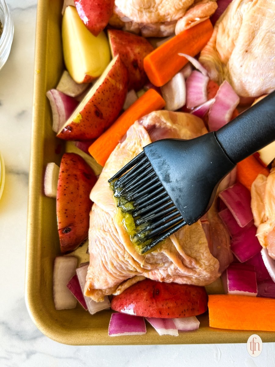 Pastry brush applying butter to raw chicken thigh.