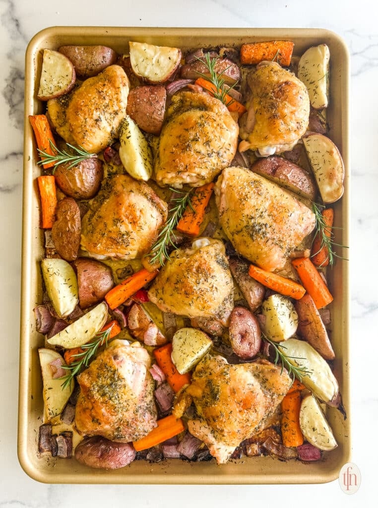 Sheet pan with cooked chicken thighs and vegetables on it.