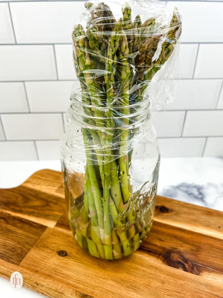 Asparagus in a glass jar covered with plastic wrap.