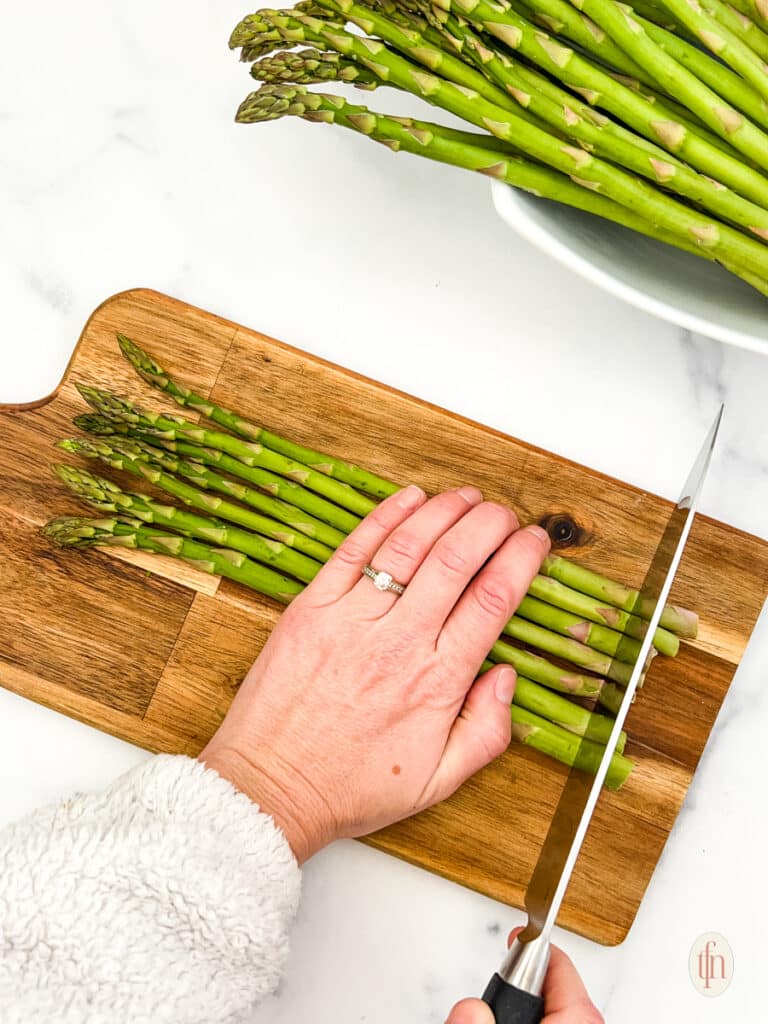 Chopping the edge of the asparagus with a chef's knife on a wooden chopping board.