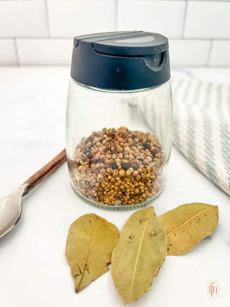Corned beef seasoning in a spice jar with spoon and bay leaves.