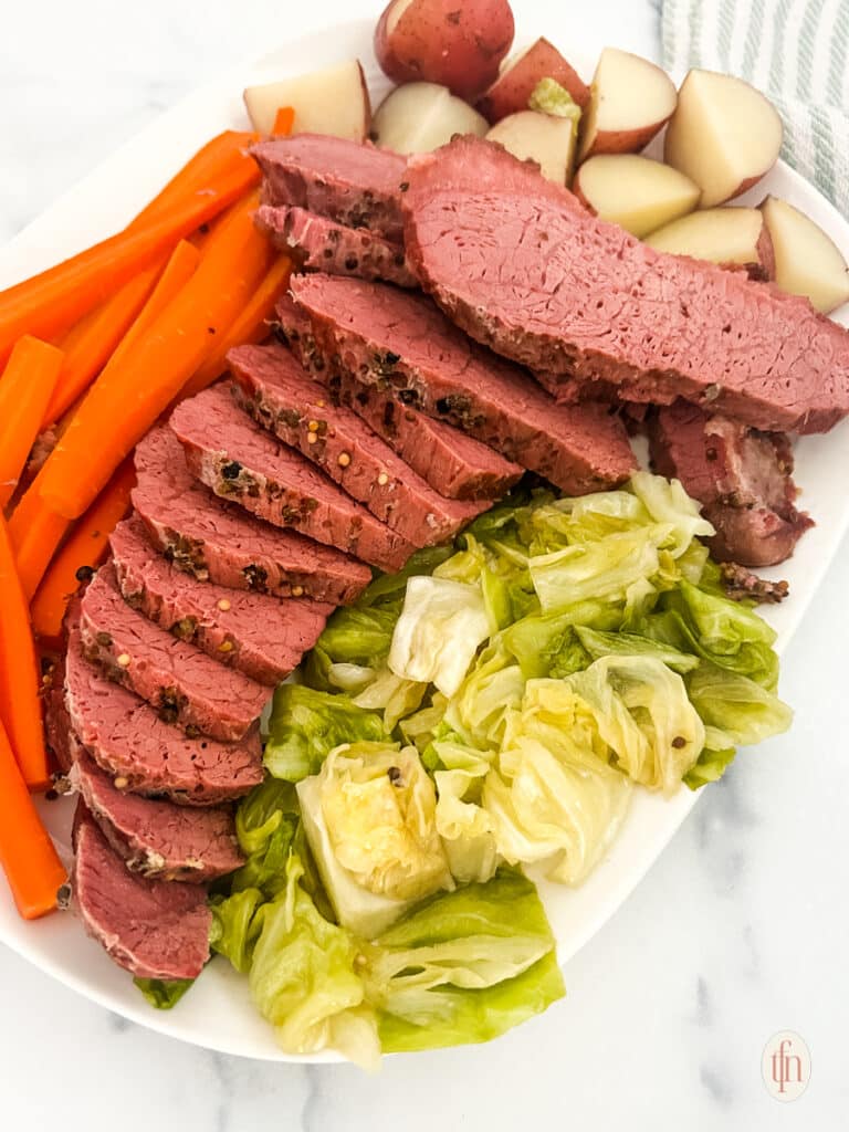 Sliced Dutch oven corned beef with vegetables on the side.