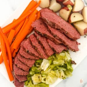Sliced Dutch oven corned beef with vegetables on the side.